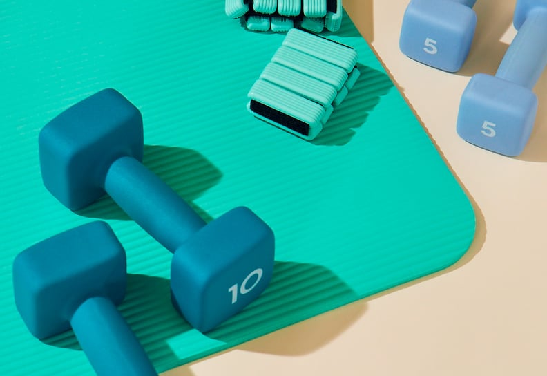 Teal yoga mat and anklet weights beside blue dumbbells.