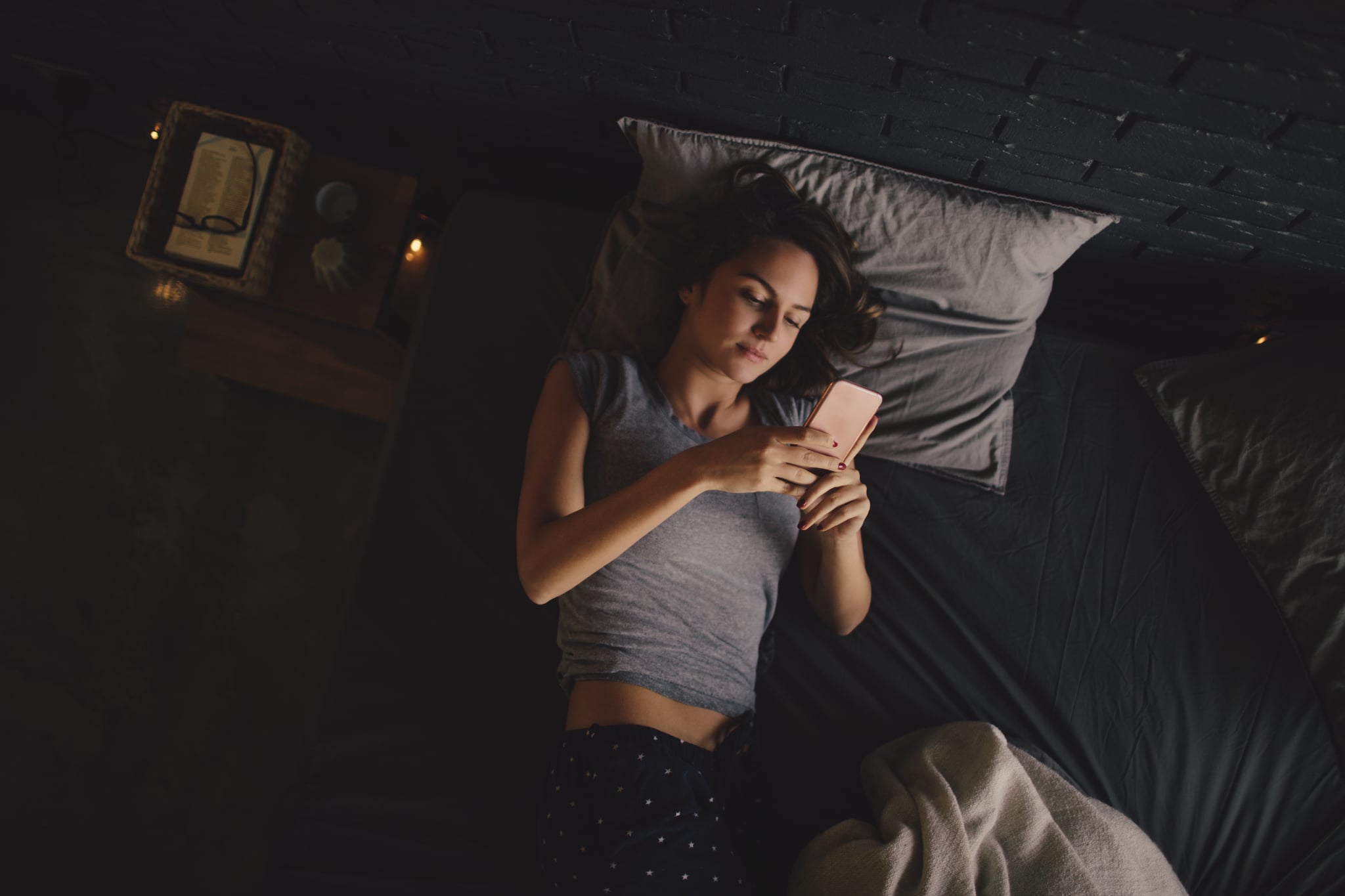 Photo of a young woman who is starting her day with a daily check up of a social media and news online, while still lying in her bed