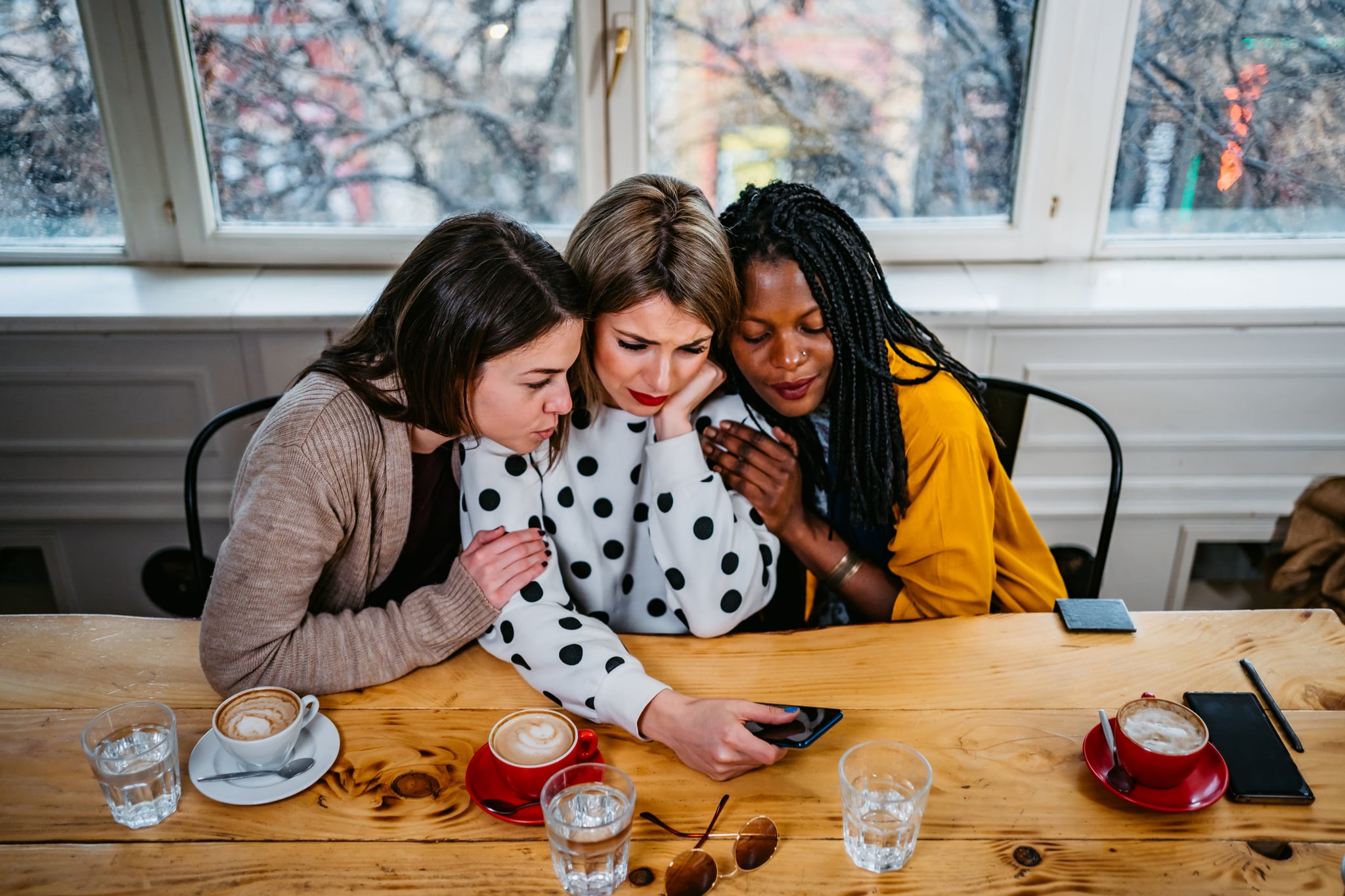 Two young women comforting their female friend in cafe.