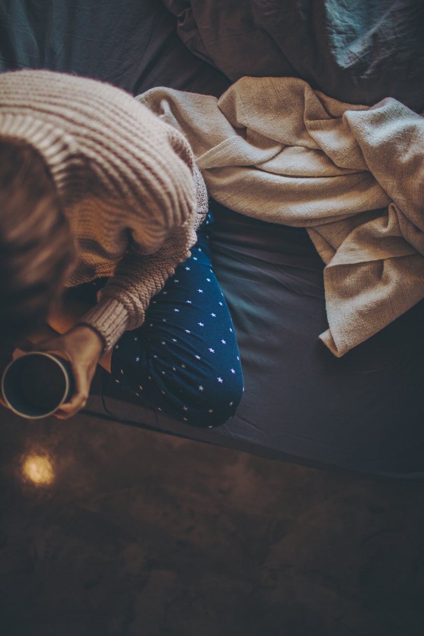 Photo of a young woman drinking her first cup of coffee still sitting in her bed, in pajamas