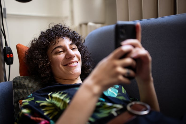 Non-binary person reading text message on phone and smiling. genderqueer person relaxing on sofa using a cell phone at home.