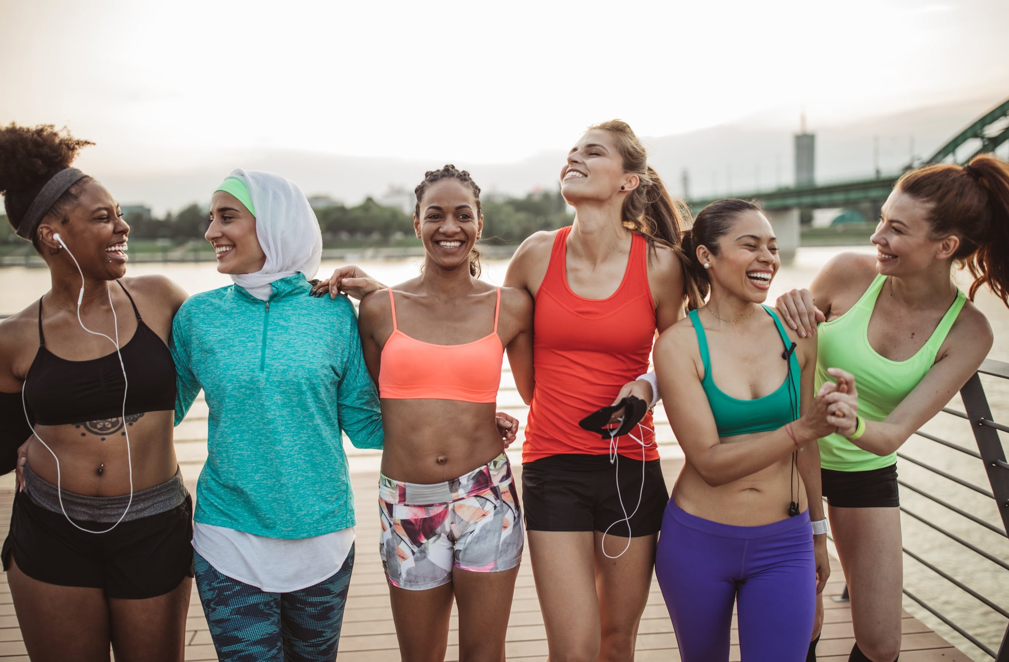 Multi ethnic group of young  women exercise outdoor, next to the river. They are wearing sport clothing, running, stretching, celebrate and support each other.