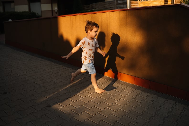 Smiling child running against the background of an orange wall near his shadow