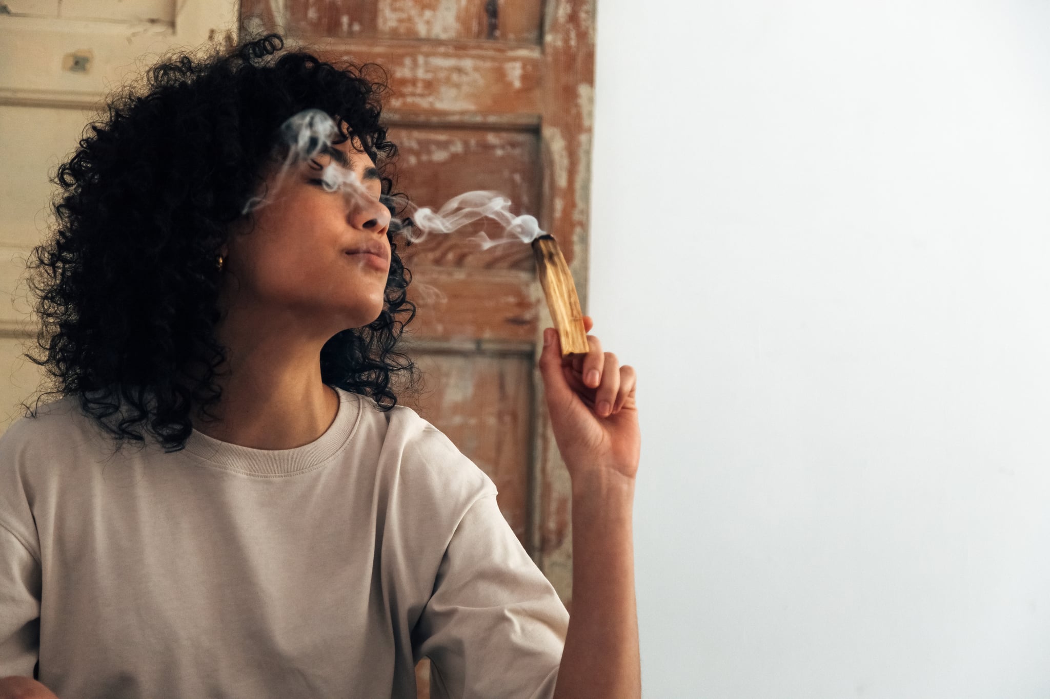 Young woman holds a smoking palo santo smudging herself and the room.