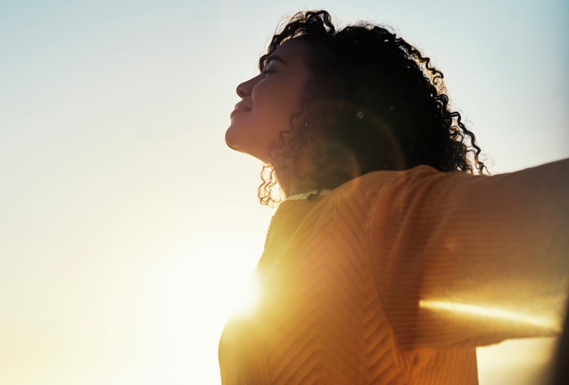 Woman outdoors during summer sunset and relax in the fresh air and sunlight, admiring the sky with freedom and flare.Mockup depicting a happy and carefree young woman relaxing outside in the morning