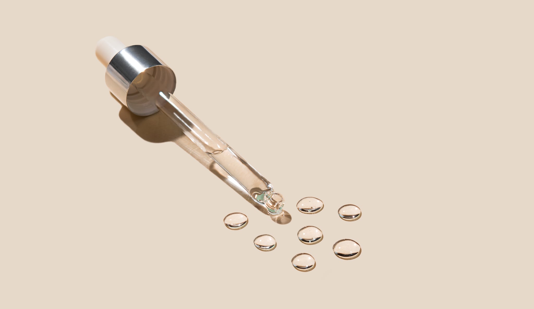 Cosmetic pipette with drops of gel on a beige background.