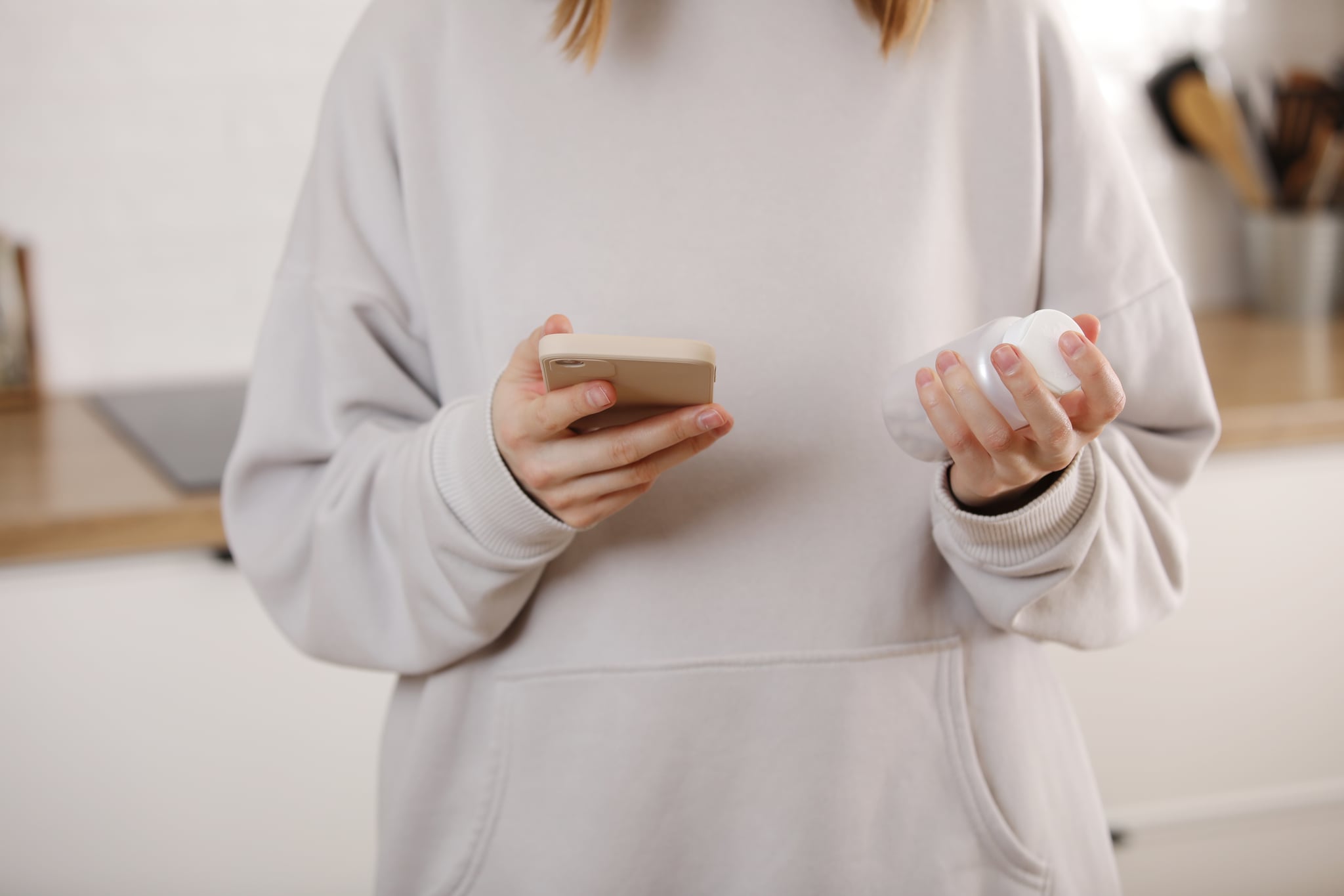 Woman Taking Medicine. Young woman Holding bottle With Pills In Hand And Reading Medical Instructions in the cellphone. Ill woman looking at medication explanation before taking prescription drugs