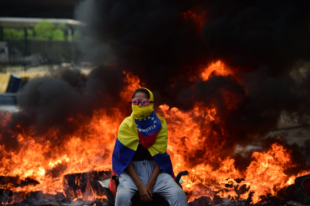 A protester remains calm as a barricade burns behind them.