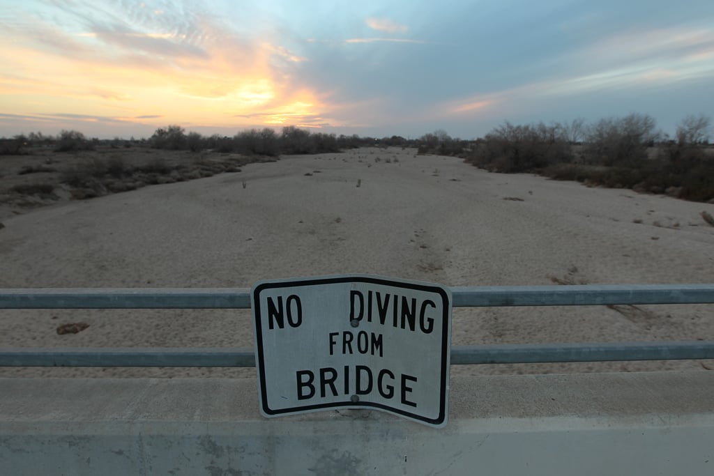 A "no diving" sign sits over the dried-up Kern River in Bakersfield, CA.