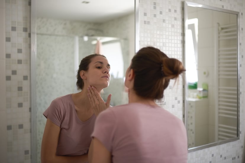 Young female in the bathroom looking in the mirror and taking care of her facial skin.