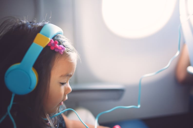 A cute 2 year old girl wearing head phones sits quietly in her seat listening to music and playing with something while flying.