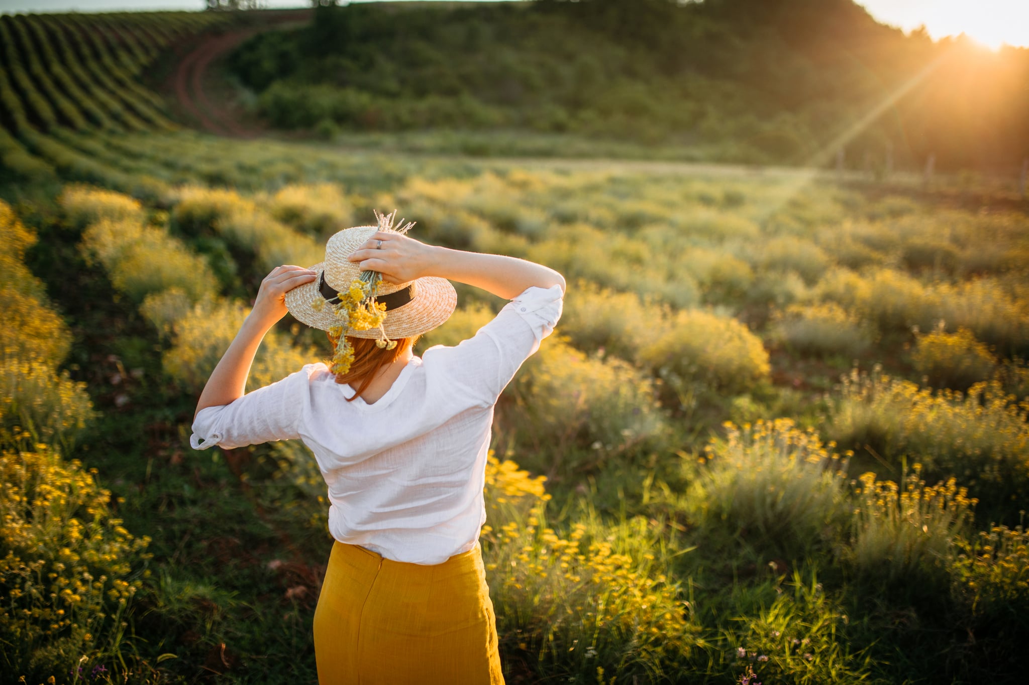 Boho style woman with hat enjoying the sunset in everlasting flowers field