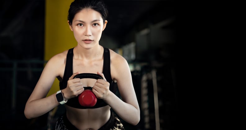 Young Asian women doing squats with a kettlebell in the gym.