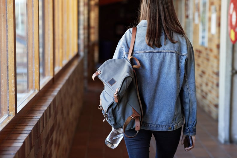 后视图的年轻女子的背包走在走廊上大学