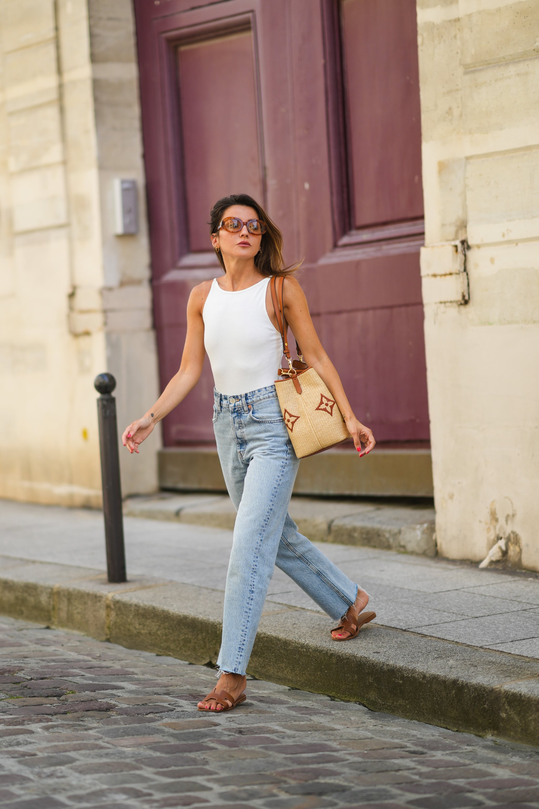 PARIS, FRANCE - JULY 20: Alexandra Pereira wears brown sunglasses from Tod's, a white ribbed tank top, a beige large wicker bag from Vuitton with printed monograms, pale blue denim ripped jeans pants, brown leather Hermes Oasis sandals / shoes, on July 20, 2021 in Paris, France. (Photo by Edward Berthelot/Getty Images)