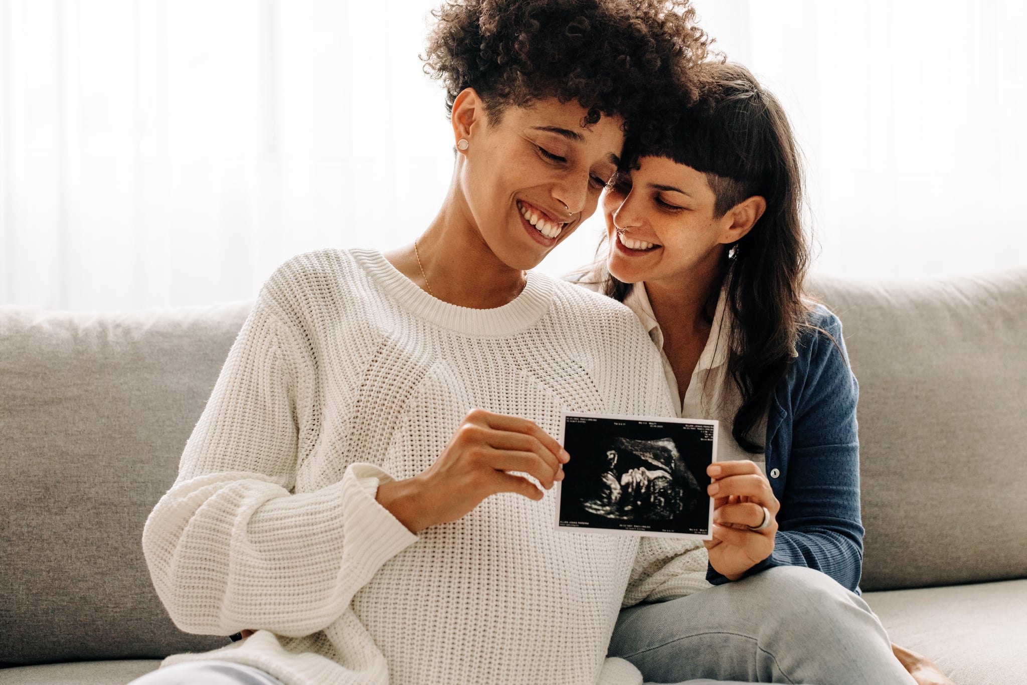 同性怀孕的夫妇拿着超声波扫描。准女同性恋夫妇微笑欣然而持有超声波检查胎儿的照片。年轻的同性恋情侣。