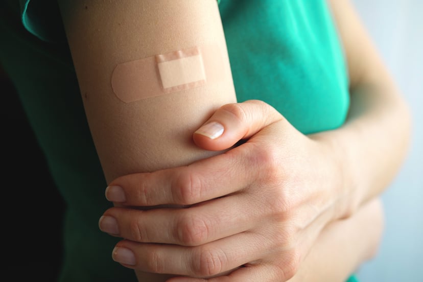 A girl or young woman holds her hand, which is covered with a patch or adhesive bandage after vaccination or injection of medication. The concept of medicine and health care, vaccination and treatment of diseases. First aid.