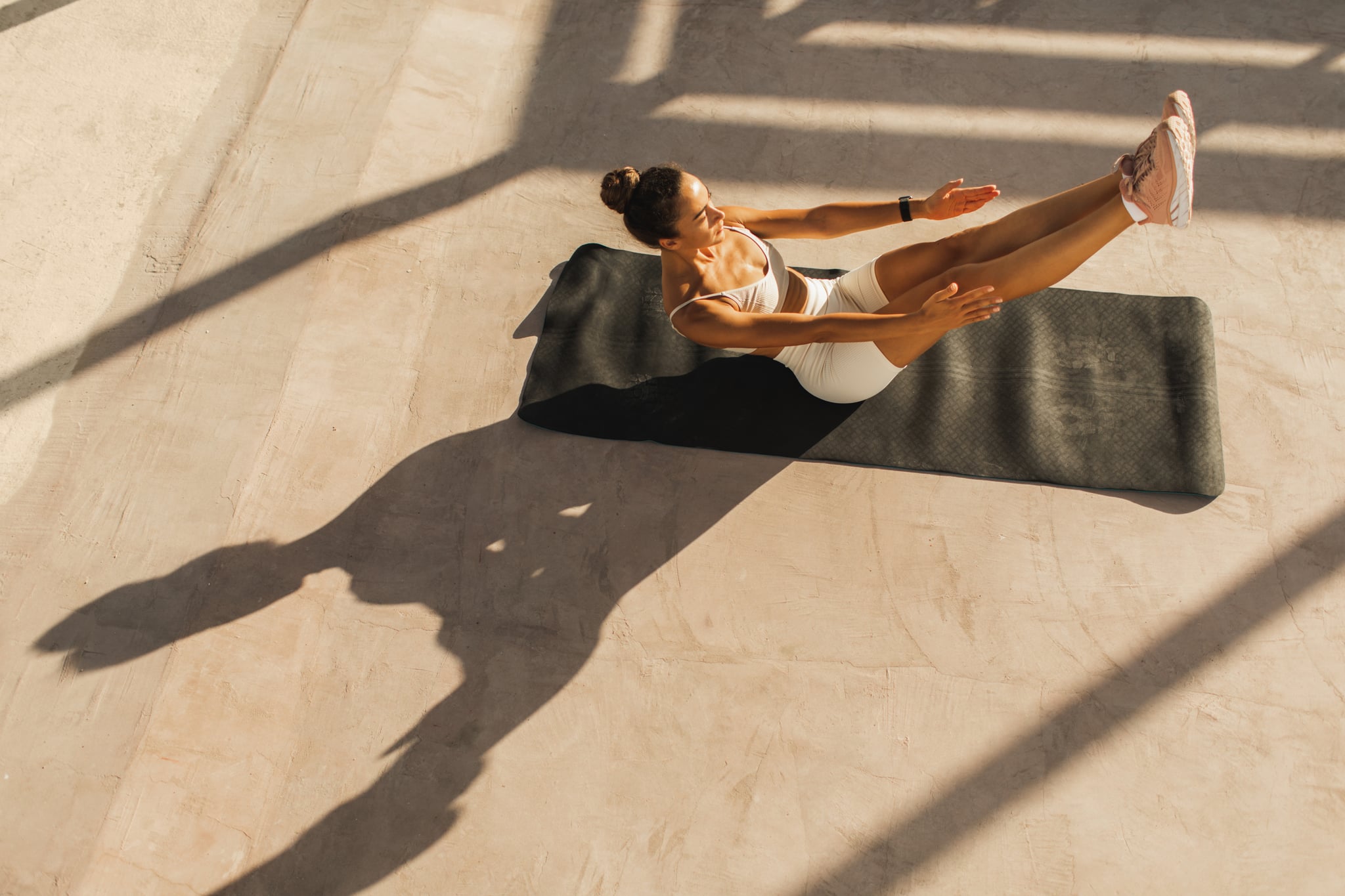 woman doing a 5-minute ab workout on a black yoga mat with a beige workout set on