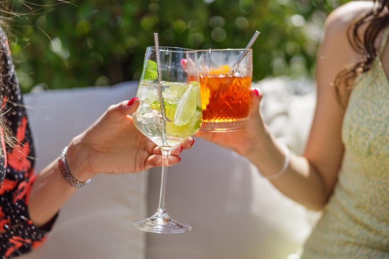 Two women proposing a toast with glasses of cocktails on ice, outdoor party on a sunny day