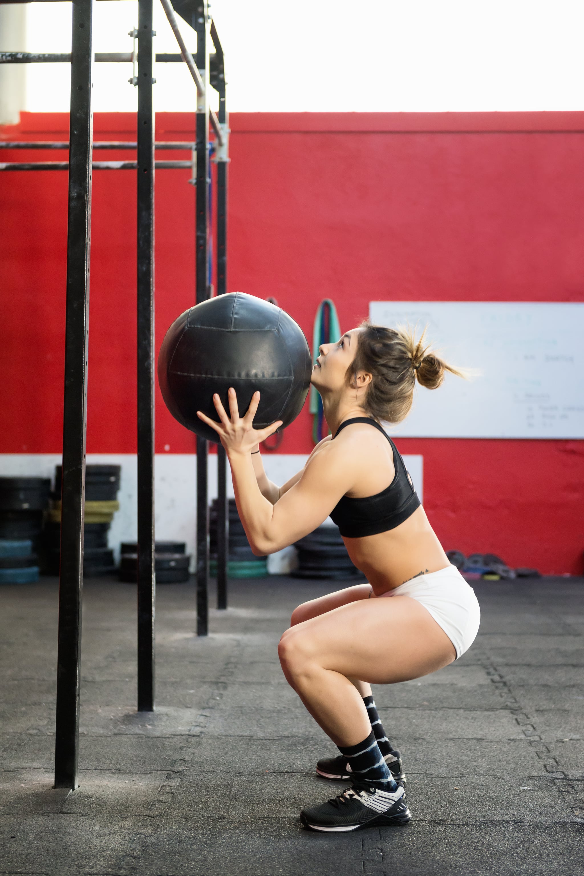 Vertical colour profile view image of muscled woman training at gym with a medicine ball.