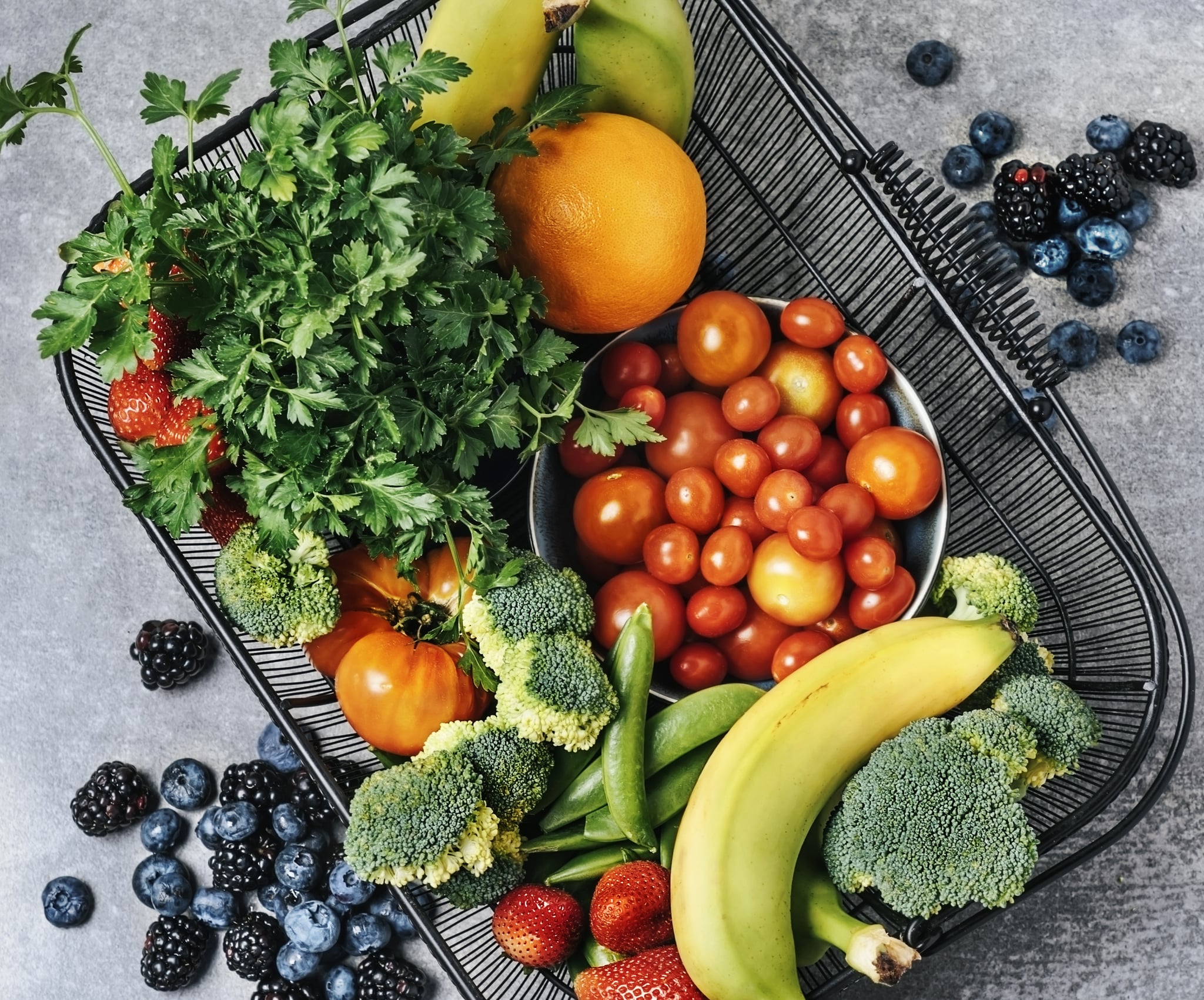 A basket of fresh vegetables, and fruits on grey background