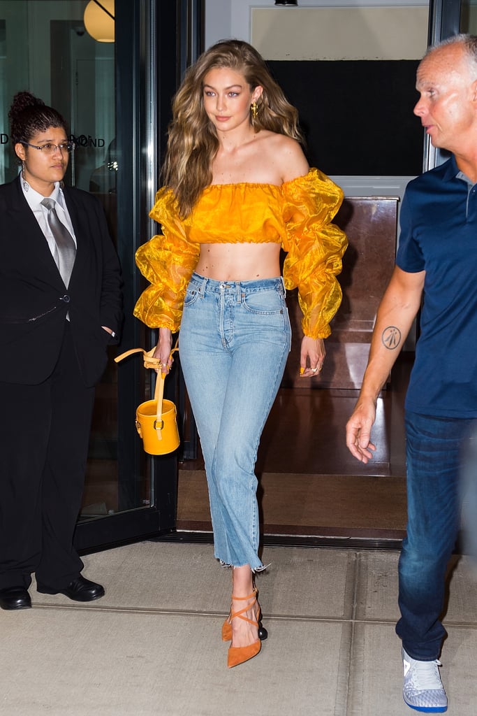 Gigi wore this sheer Bardot top with a pair of Re/Done jeans to an event celebrating her V Magazine cover. She accessorized with orange heels and a matching round purse.