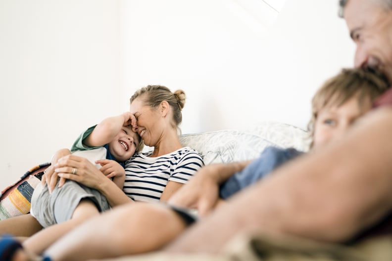 A photo of smiling family relaxing on sofa. Happy parents are embracing sons. They are wearing casuals at home.