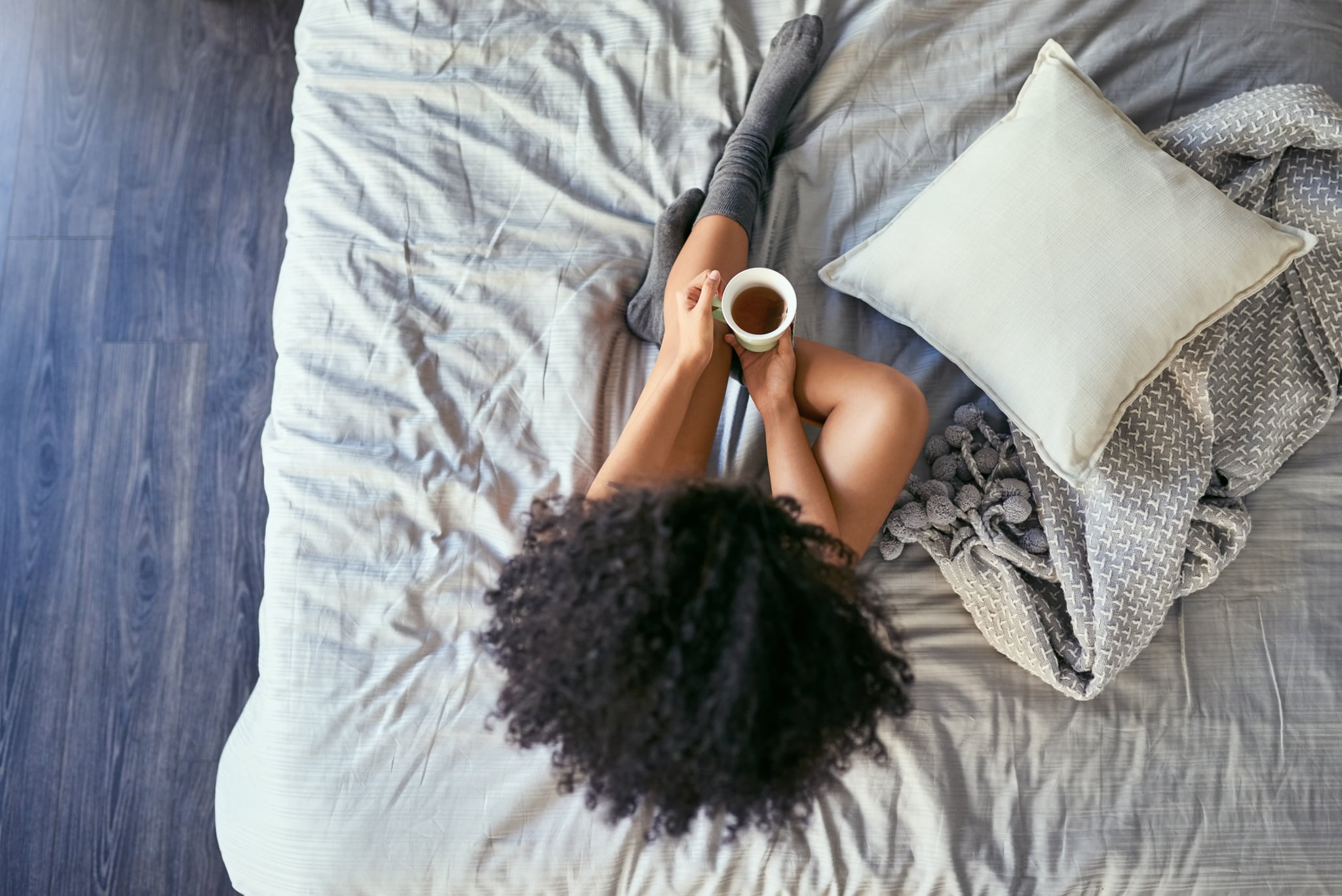 High angle shot of a young woman relaxing on her bed in the morning and drinking tea