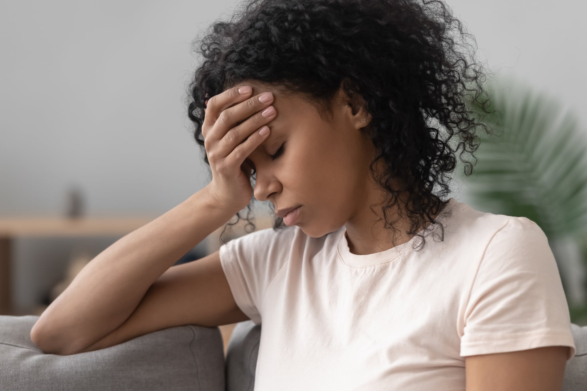 Close up african female sit on couch feels unhappy desperate thinking about personal difficulties mental health problems, 30s sad woman need psychological support goes through divorce break up concept