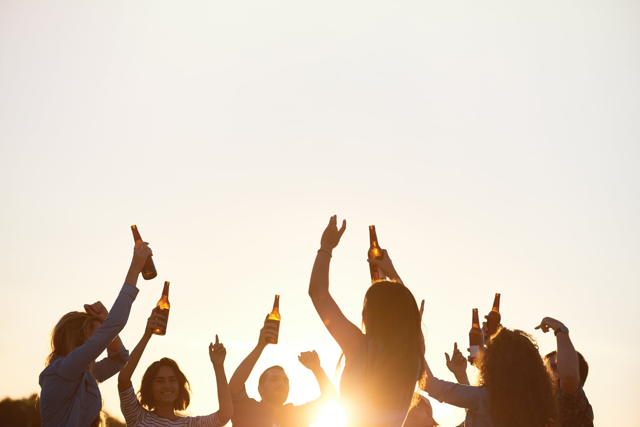 Happy friends dancing at outdoor concert and drinking beer during all night