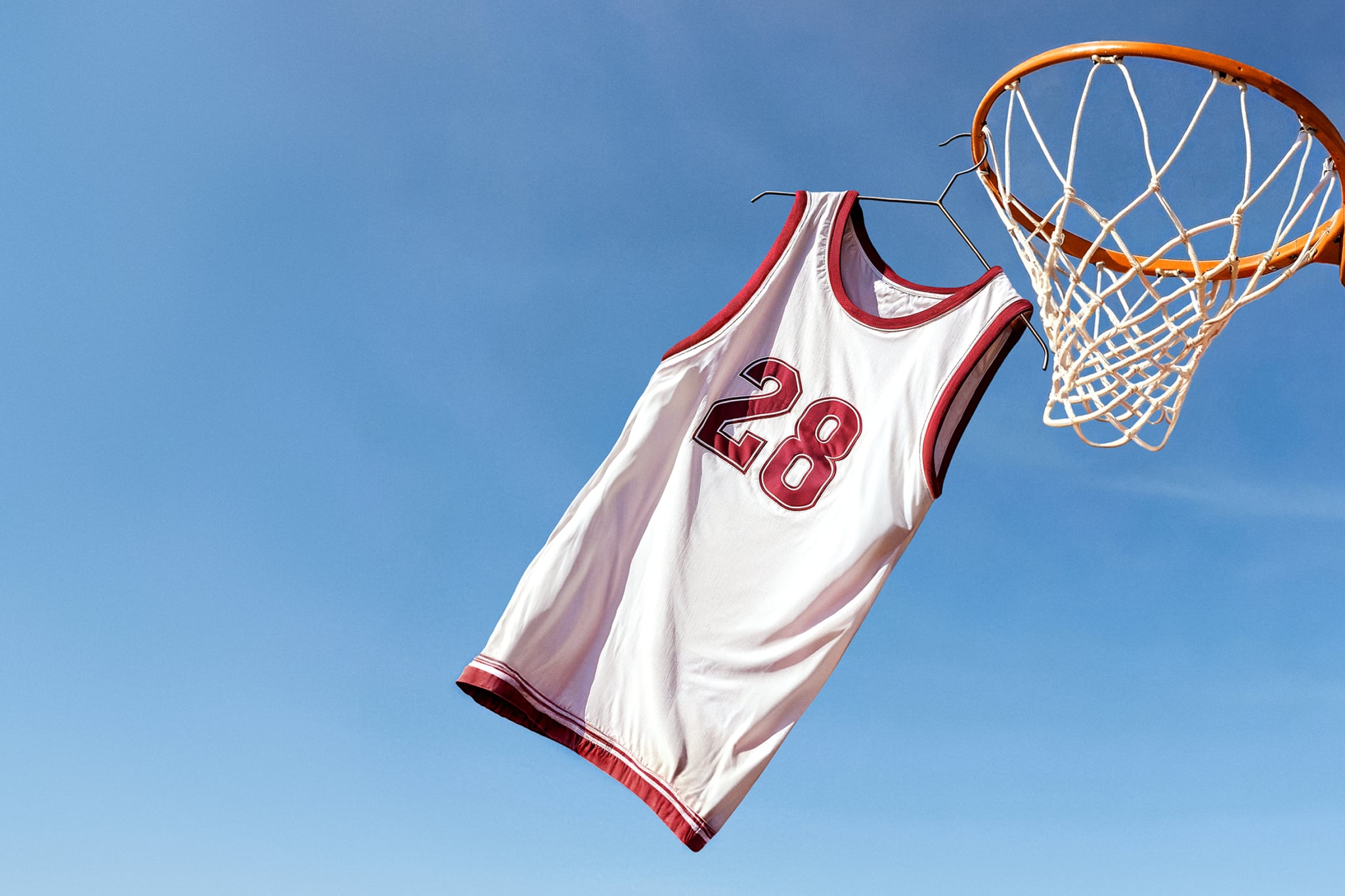 Basketball jersey hanging by a clothes hanger from a basketball net, against a blue sky