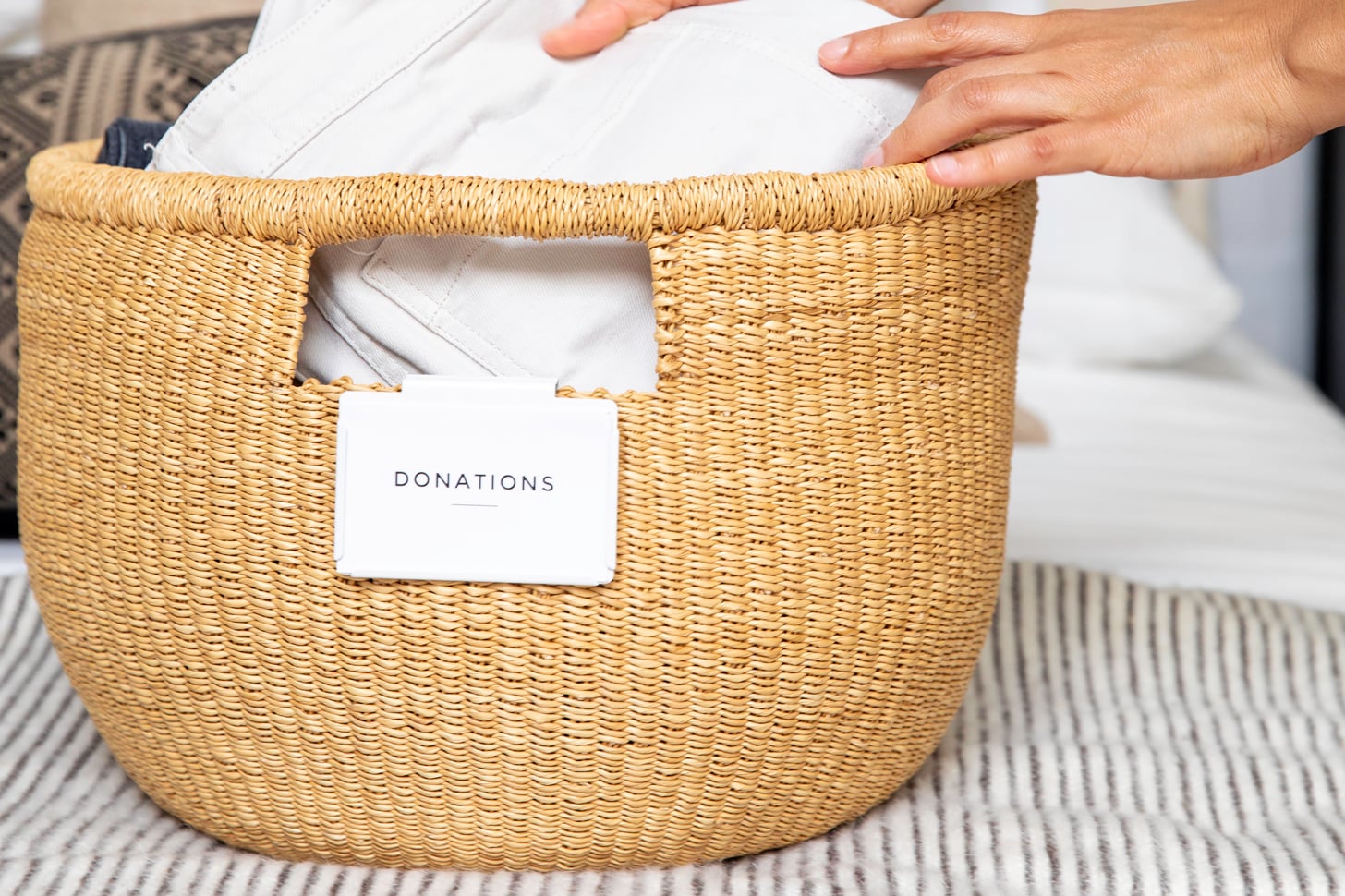 hands placing pants into a woven basket labeled donations