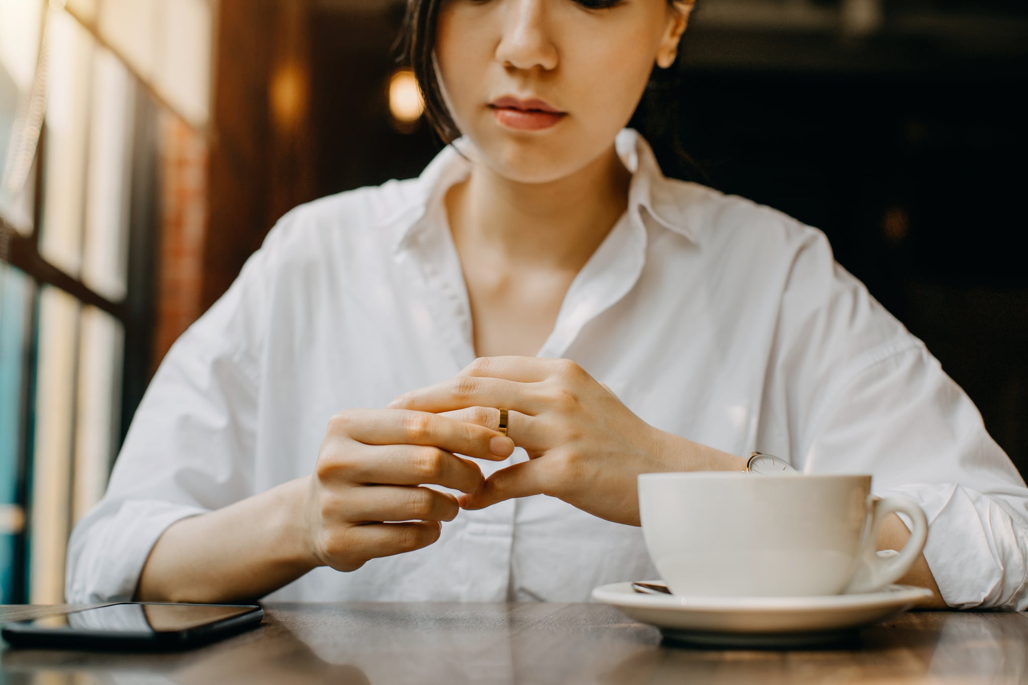 女人一边喝咖啡，一边在咖啡厅等待，紧张地摸着手指上的结婚戒指