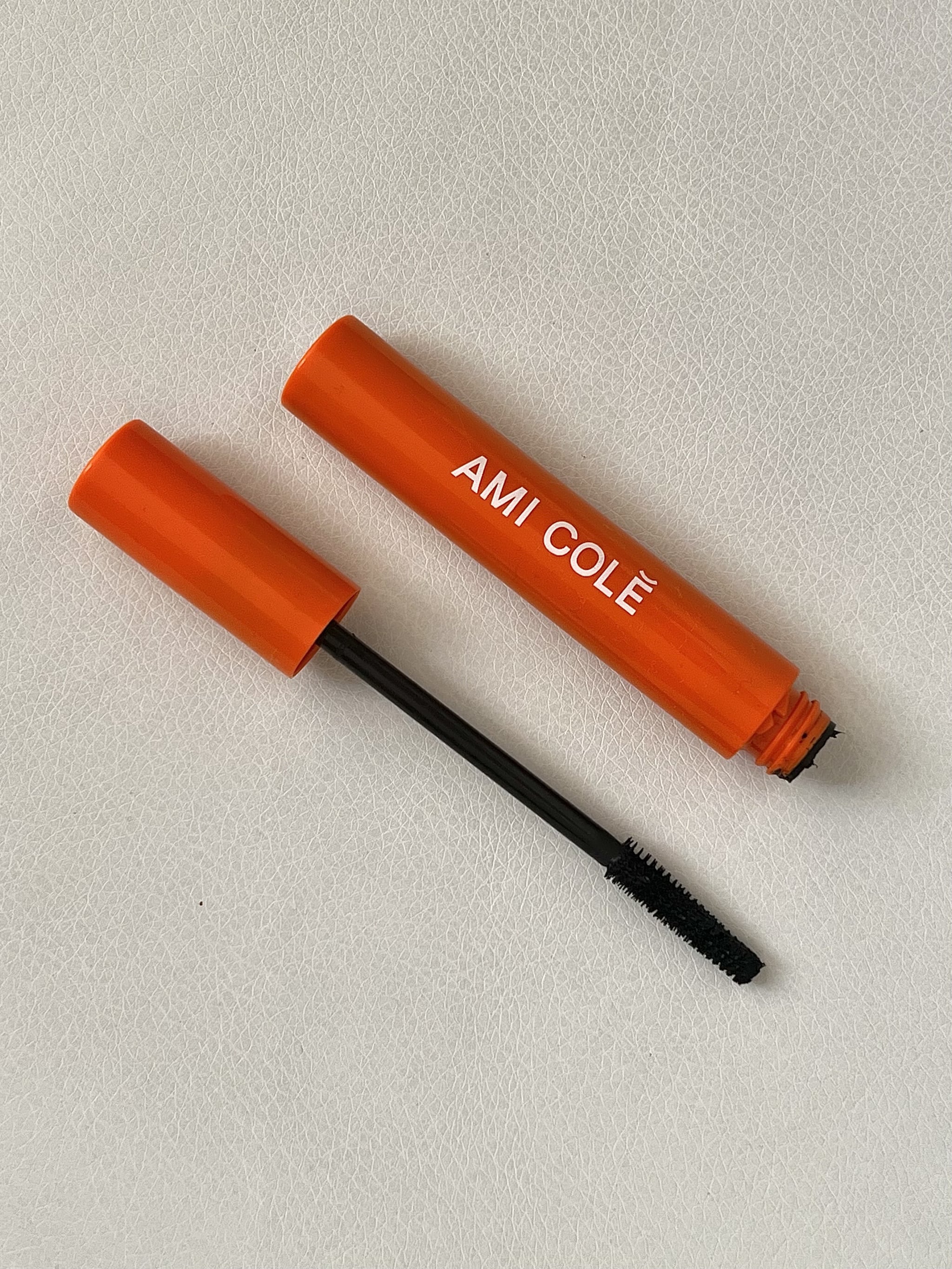 The Ami Cole Lash Amplifying Mascara with cap open and mascara wand showing. The wand is thin and tapered with densely packed bristles.