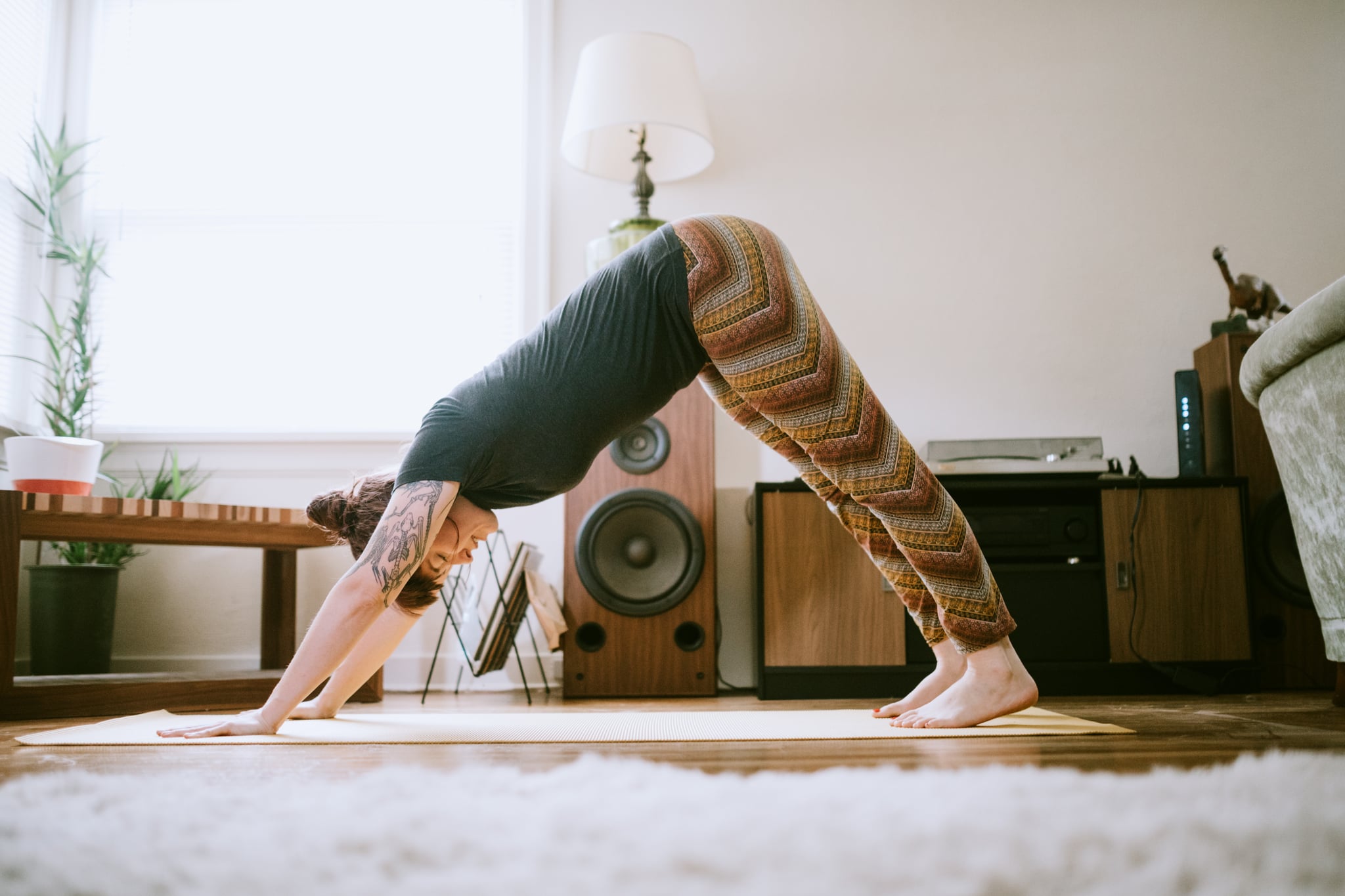 A cheerful woman enjoys performing yoga stretches and exercise routines in her living room, the sun shining brightly through the windows.