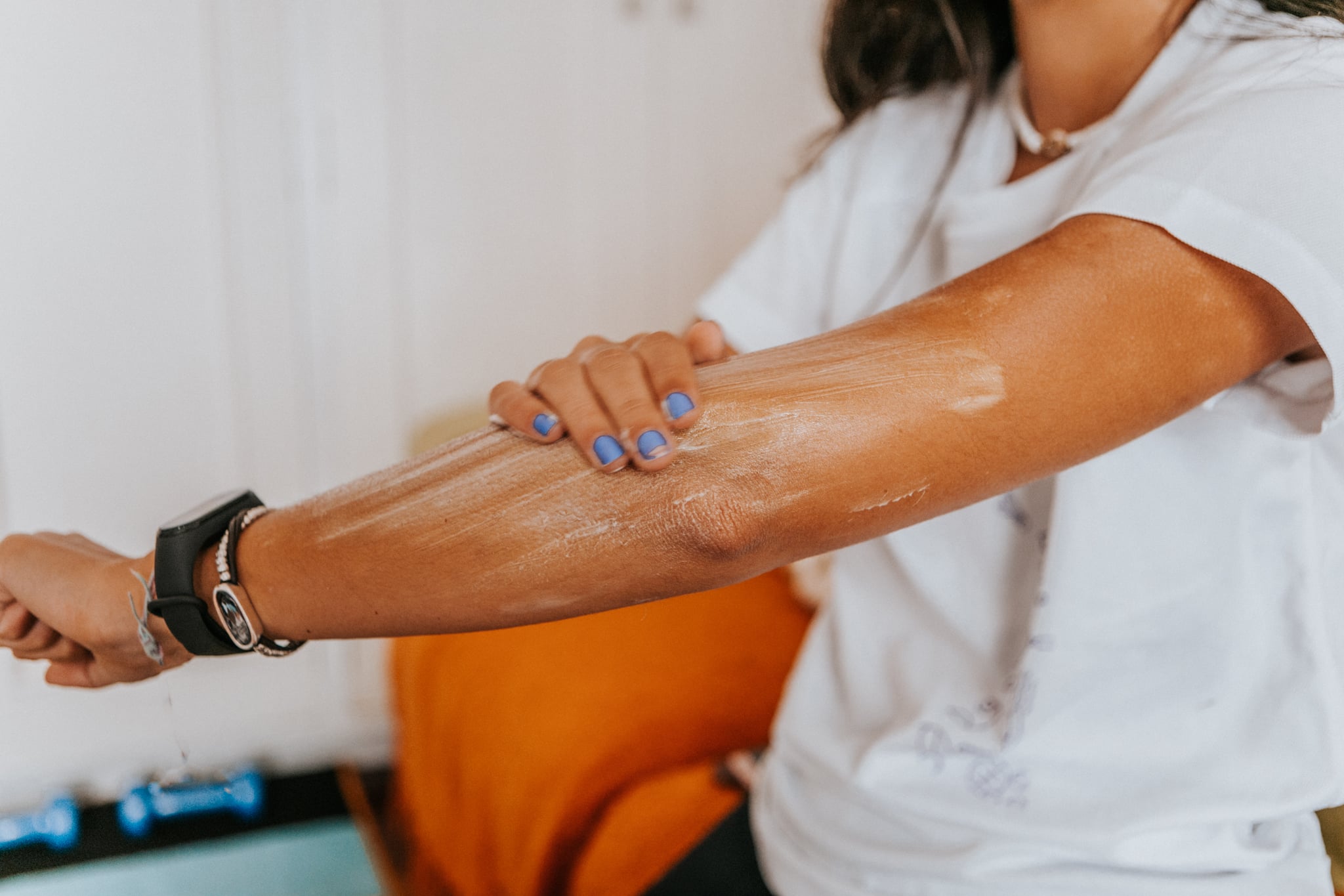 medium shot of young woman in casual clothes applying cream on arms