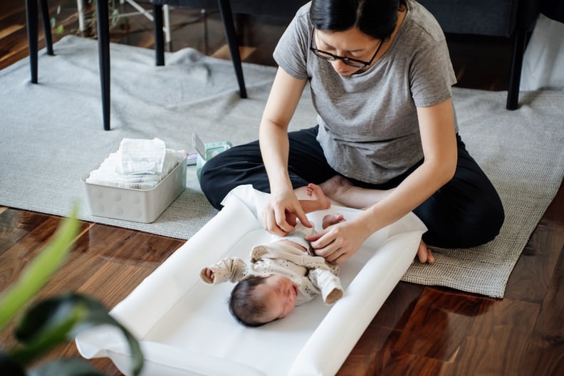 Young Asian mother changing the diaper for her newborn baby, finding meconium (baby's first poop), on the floor at home