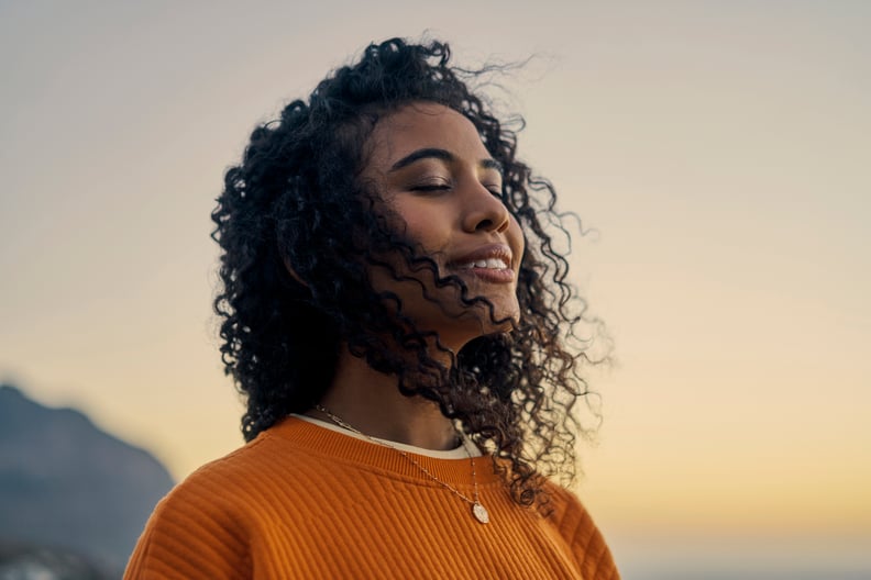 Woman standing outdoors with her eyes closed and a peaceful expression on her face. Sunset in the background.