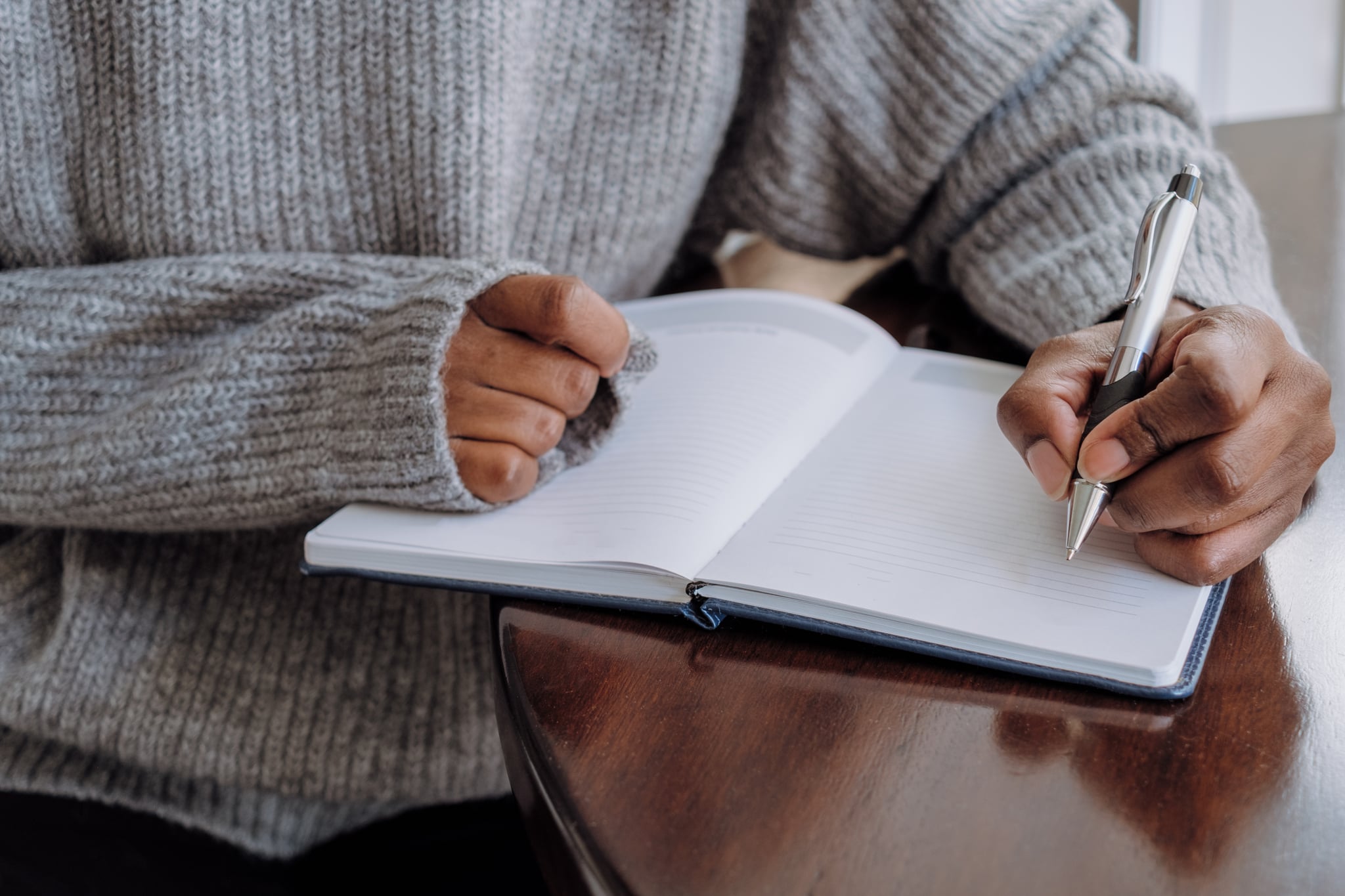 Close-up of unrecognizable black woman writing in journal while sitting at table Close-up of unrecognizable black woman writing in journal while sitting at table