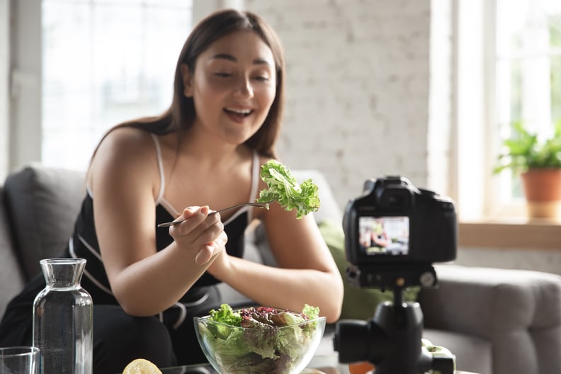A wellness influencer uses a camera to film herself eating a salad.