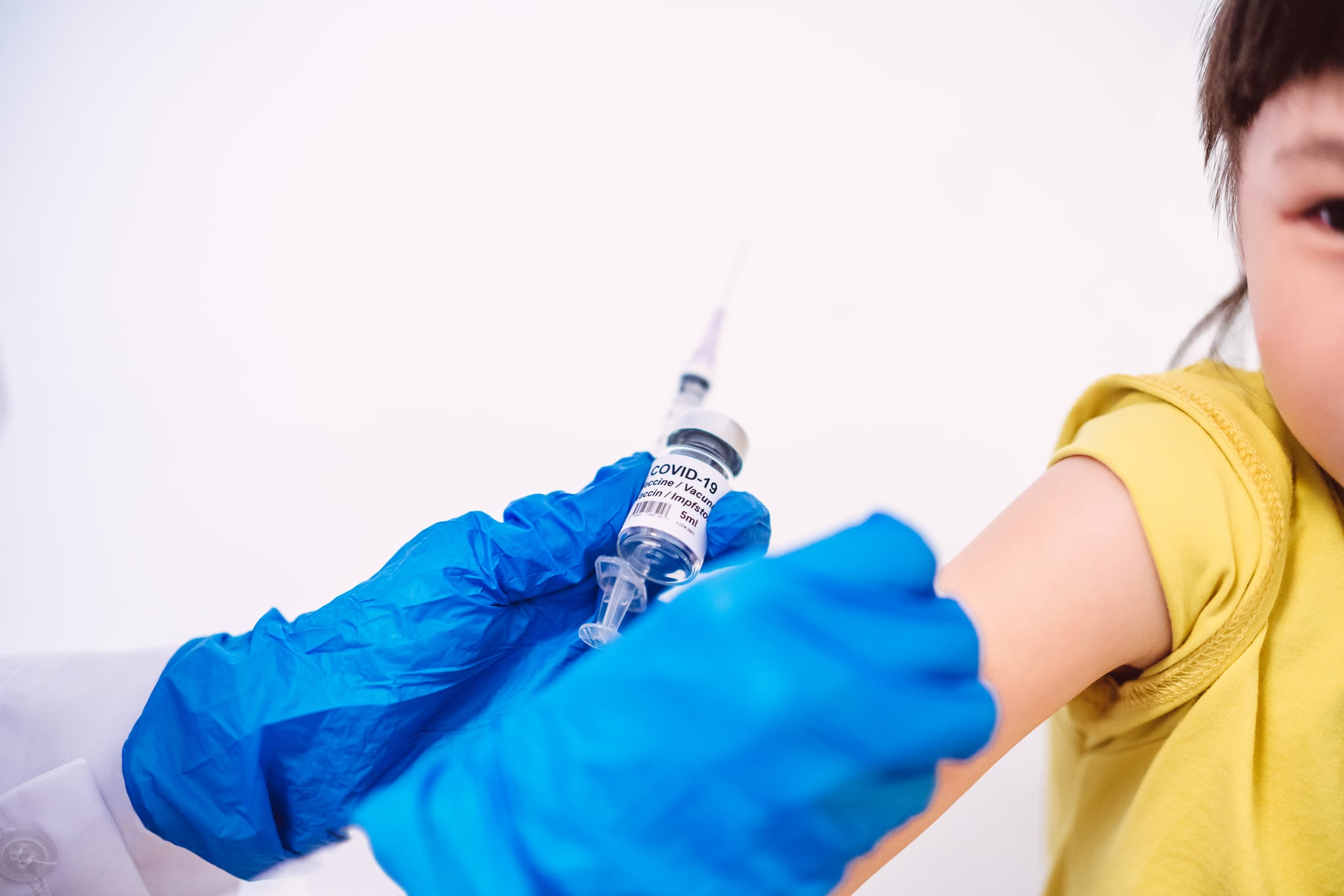 Medical doctor in protective gloves giving a kid girl Covid-19 coronavirus vaccine.