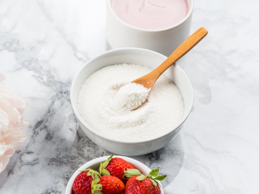 Collagen protein powder in bowl with wooden spoon on marble table. Adding collagen supplement to strawberry yogurt. Angle view