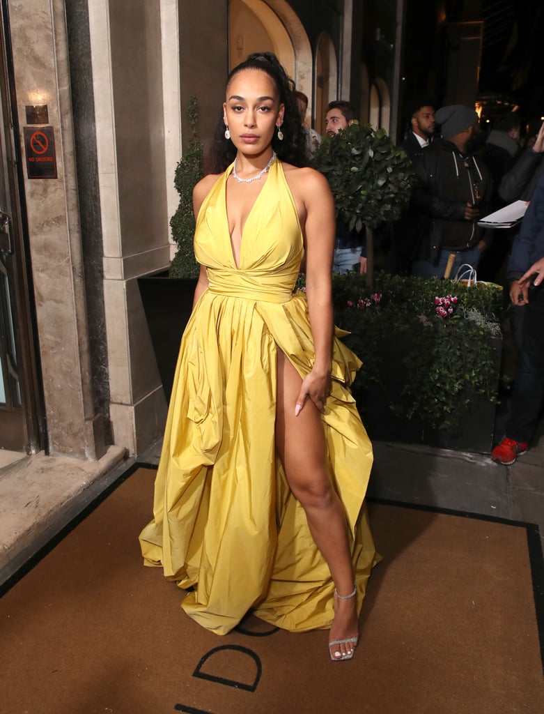 We should all practice curtsying for Jorja Smith because she just staked her claim as fashion royalty. The 22-year-old singer showed up to the Harper's Bazaar 2019 Women of the Year awards on Oct. 29 looking like the complete Disney princess package — sparkling jewels included. 
She accepted her musician of the year plaque while wearing a golden halter gown with a bustle in the back that would make Princess Belle proud, plus a modern-day upgrade in the form of a sexy hip-high slit and plunging neckline. Jorja tied the ensemble together with sparkling silver heels and complementary glittering jewelry, and wore minimal makeup with her hair in a high ponytail. A yellow ballgown might be a tale as old as time, but her take is refreshing beyond belief. Keep reading to see more glimpses of Jorja's look from all angles.