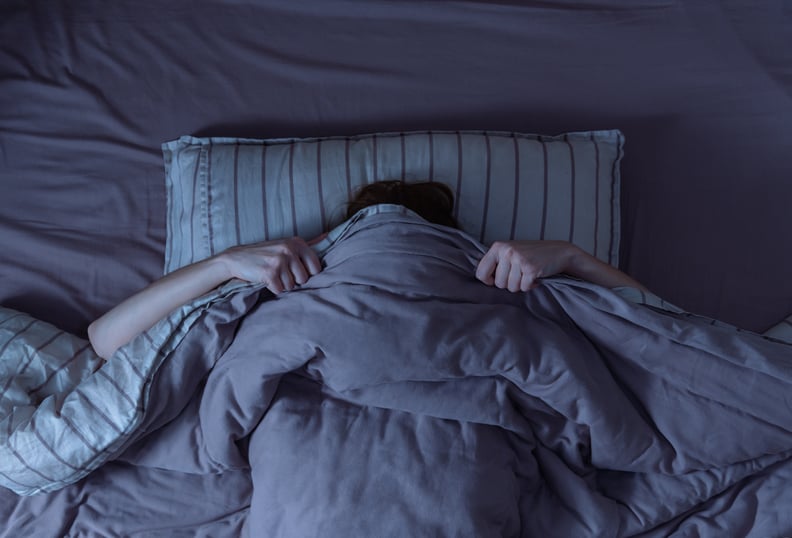 Top view of scared woman in bed covering her face with blanket.