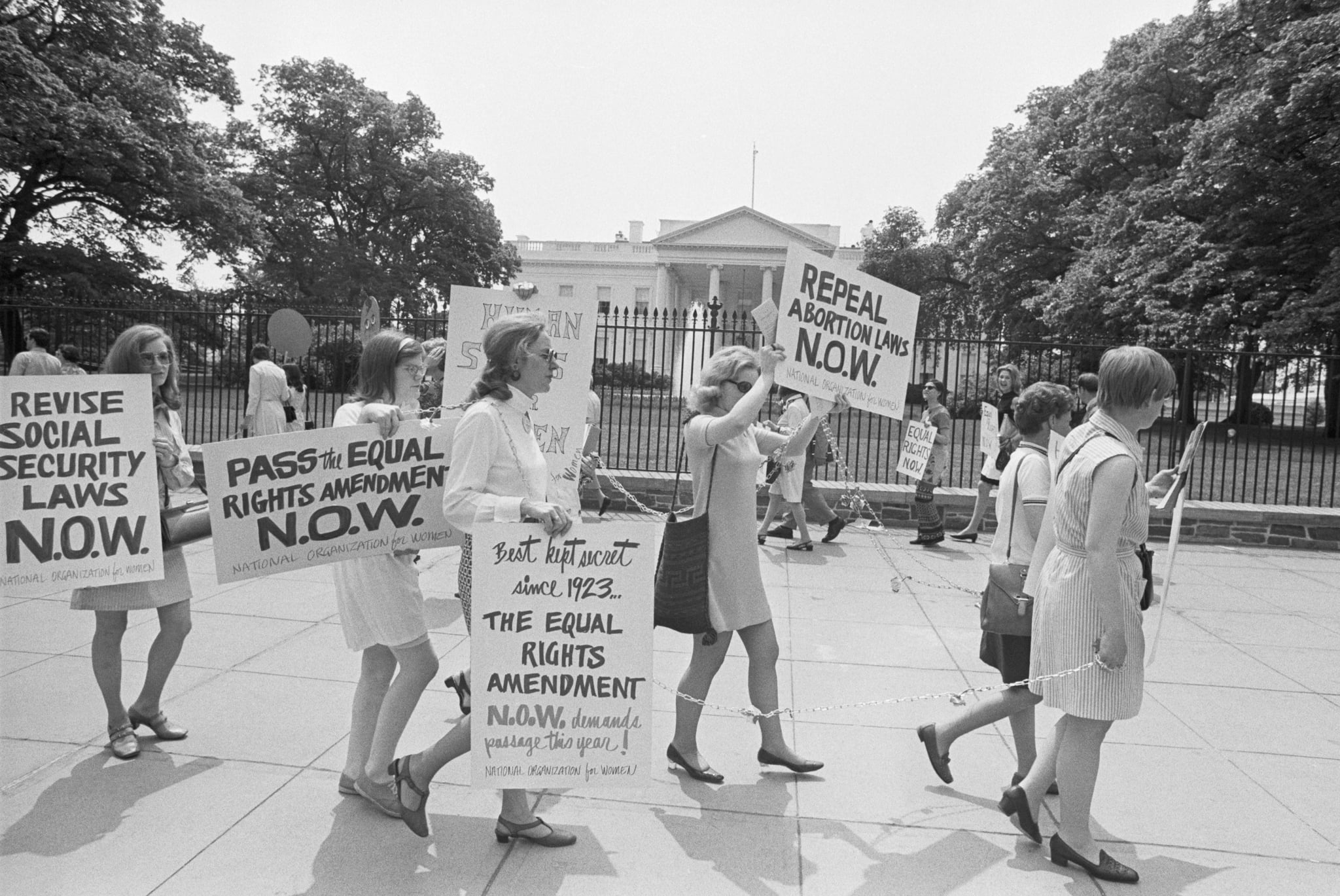 Members of the National Organization for Women demonstrate outside the White House. They wear chains decorated with flowers, and are asking for passage of the Equal Rights Amendment.