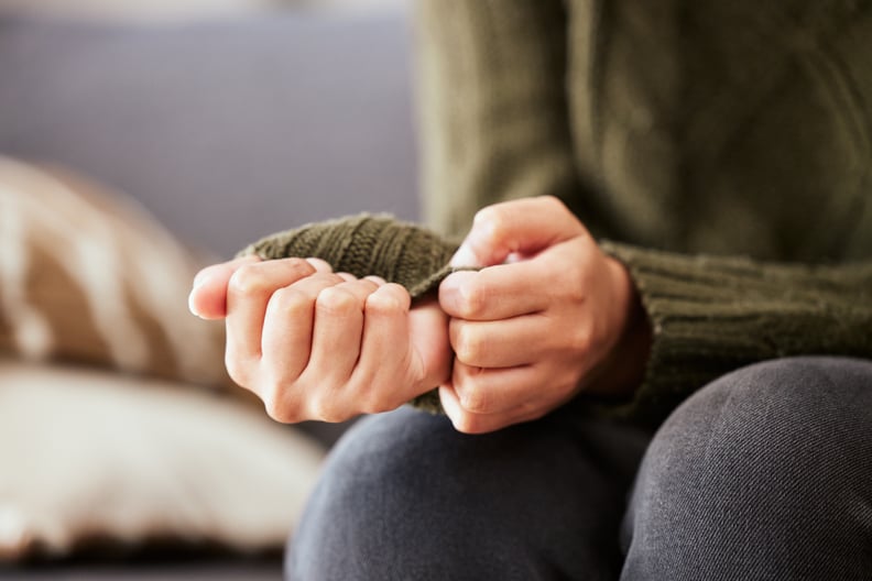 Unidentifiable woman anxiously pulling on the sleeves of her green sweater.