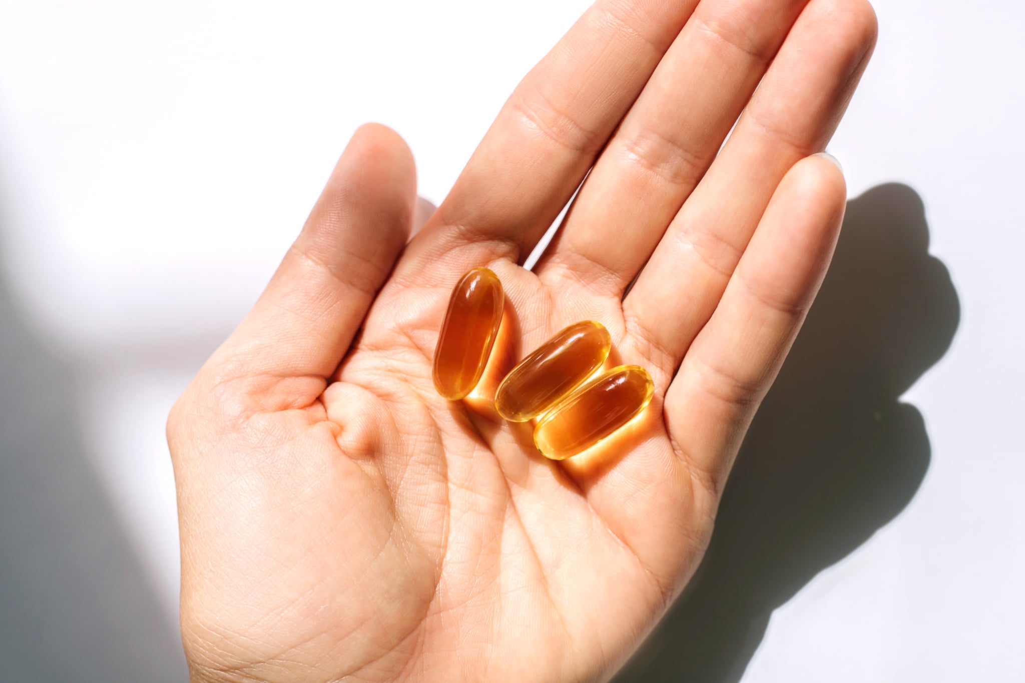 Woman's hand holding fish oil supplements on white background. Close-up.