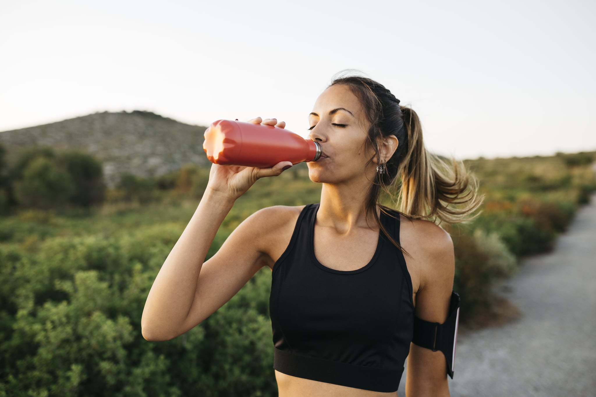 Fit young Woman in black sportswear drinking water from a reusable metal bottle after running workout: can you drink too much water?