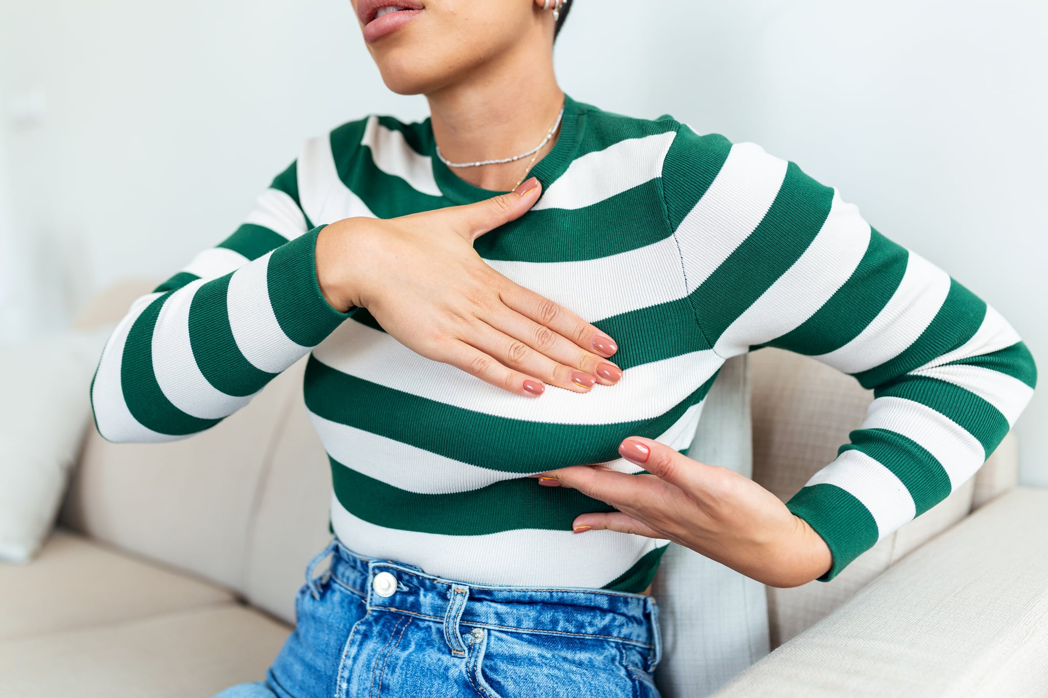 Young woman palpating her breast by herself showing concern about breast health.