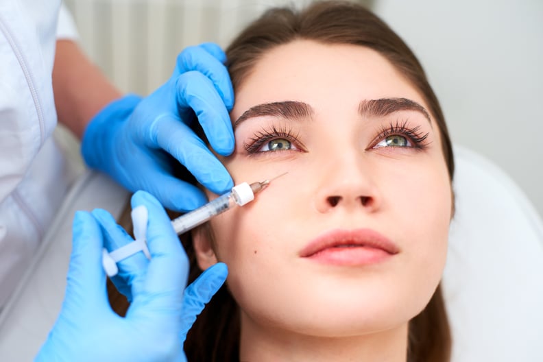 Beautician doctor in medical gloves with syringe injects botulinum under eyes for rejuvenating wrinkle treatment. Filler injection for under eye wrinkles smoothing. Plastic aesthetic facial surgery in beauty clinic